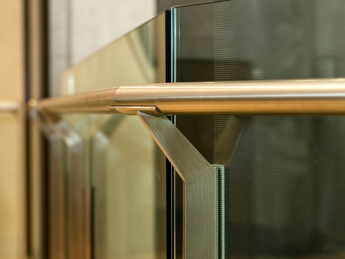 Champagne-gold brushed metal elevator handrail bracket on a glass panel