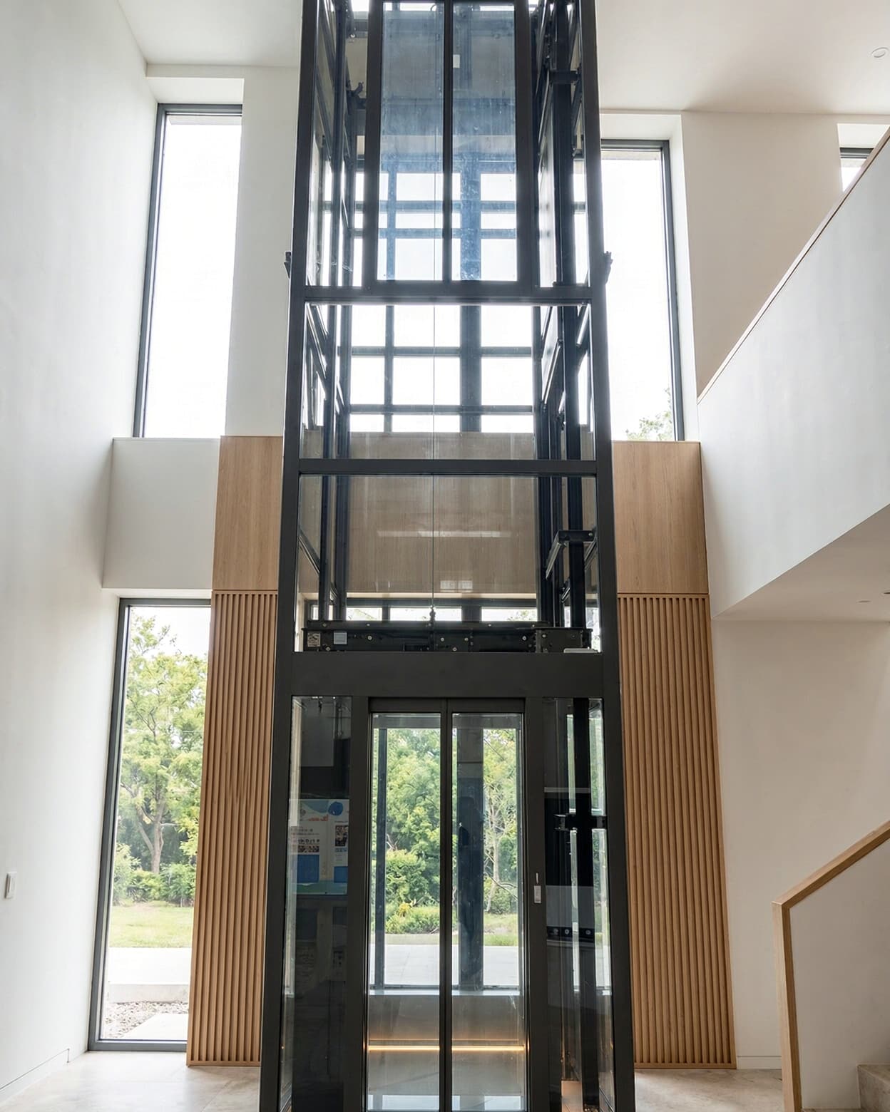 A SINNVO glass-shaft elevator with a black steel frame rising through a double-height villa hall